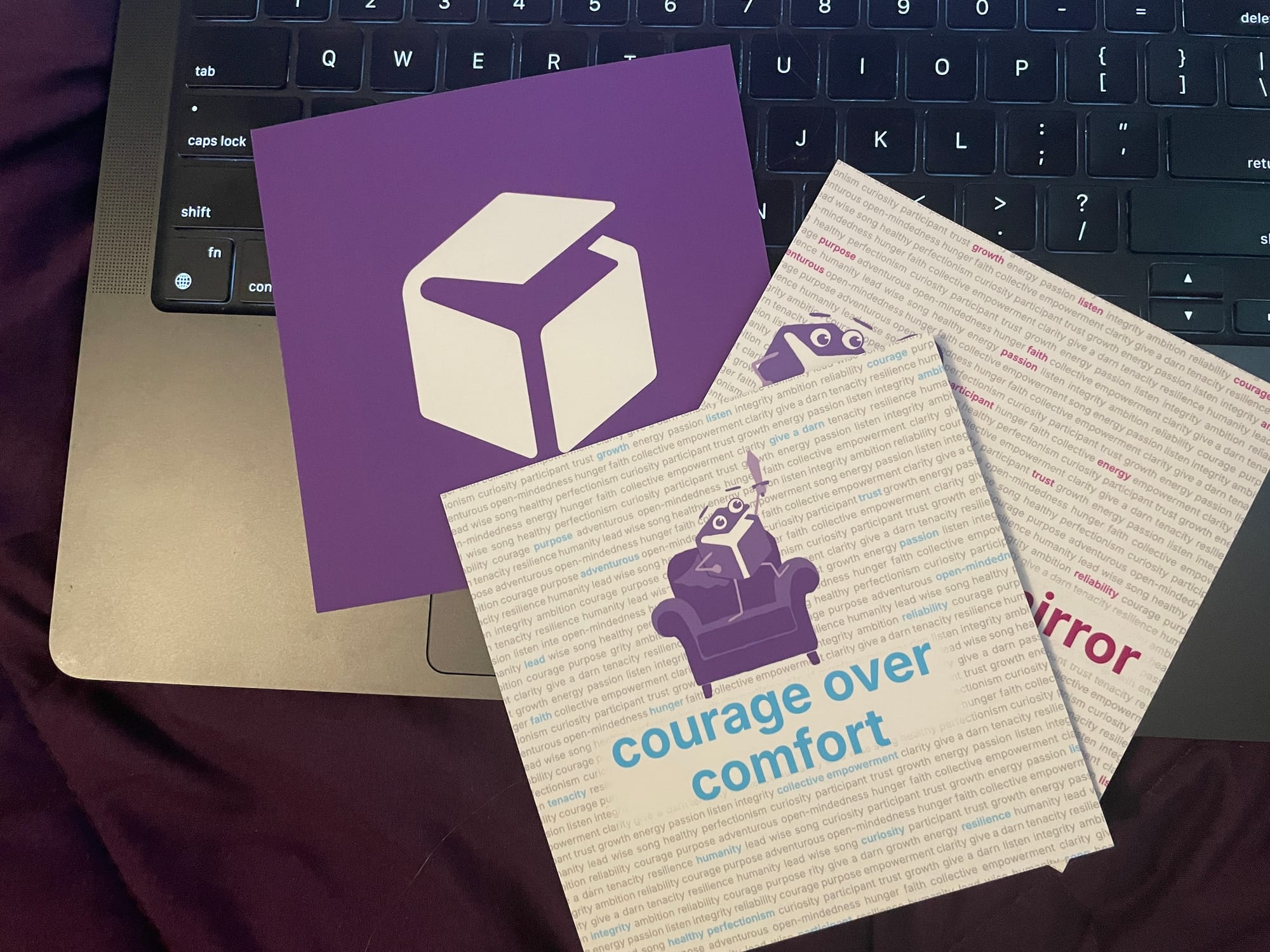 three cards sitting on a laptop keyboard; one shows the RunPod logo. The top card says "courage over comfort."